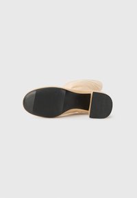 Suela de zapato de goma en color melocotón con una sección texturizada negra y ranuras para mayor agarre, con un diseño suave y curvado y un ligero tacón.