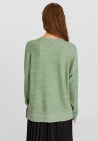 Pull vert tricoté à coupe ample, col rond et ourlet côtelé. Texture lisse, design uni et manches mi-longues.