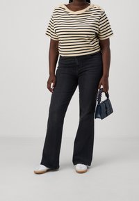 Striped beige and navy short-sleeve top with button accents, paired with flared dark jeans and white sneakers. Holding a blue handbag.