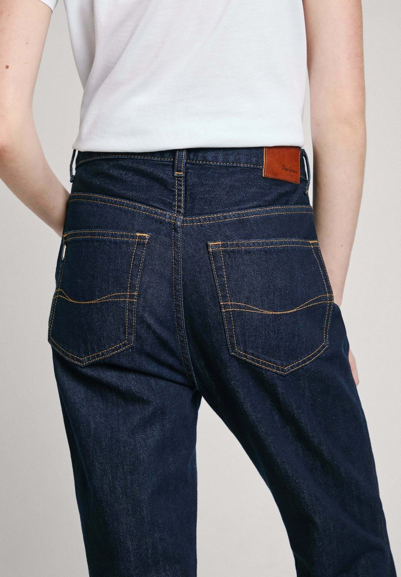 Dunkelblaue Jeans aus Denim mit orangefarbenen Nähten, ausgestattet mit einem Lederpatch am Bund und zwei Gesäßtaschen mit geschwungenen Nähten.