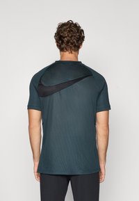 Tumši zilā krāsā sporta krekls ar īsām piedurknēm, ar melnu Nike logo aizmugurē un tekstūru, kas nodrošina elpojamību.