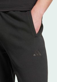 Schwarze Sweatpants aus weichem Material, ausgestattet mit einer Seitentasche und einem dezenten, gestickten Drei-Streifen-Logo am unteren linken Bein.