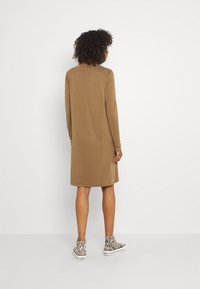 Långärmad brun klänning med rak skärning, tillverkad av mjukt tyg, i kombination med mönstrade sneakers som går upp till anklarna. Enkel och avslappnad design.