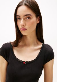 Svart topp med en texturerad design, korta ärmar och en litet räfflad spetskrage med en liten rosdetalj.