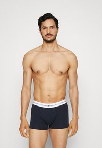 Marineblaue Baumwoll-Boxershorts mit einem weißen elastischen Bund, der das Logo "TOMMY HILFIGER" trägt. Glatte Textur, enganliegendes Design. Keine zusätzlichen Muster.