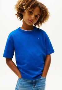 T-shirt in cotone blu con maniche corte e scollatura rotonda. Presenta un piccolo logo sul petto. Indossato con jeans in denim azzurro chiaro.