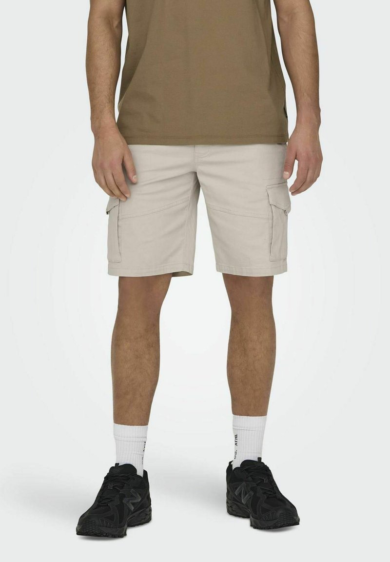 Beige cargo shorts med flere sidelommer, lavet af bomuld. Kombineret med en brun t-shirt, sorte sneakers og hvide sokker.