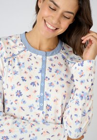 Sudadera de mangas largas con un cuello azul claro y una lista de botones, que presenta un patrón floral en tonos rosa pastel y azul sobre un fondo crema.