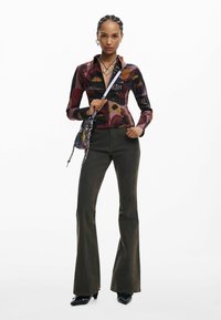 Cămașă cu mânecă lungă cu model multicolor, blugi evazați închiși la culoare cu detalii cusute, cizme negre cu vârf ascuțit, geantă mică de purtat peste umăr.