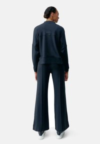 Set coordinato blu navy composto da un pullover a vestibilità ampia con scollo rotondo e pantaloni a gamba larga. Tessuto morbido e dettagli di cucitura sottili.