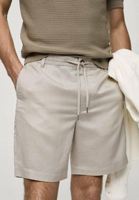 Shorts en lin beige avec une taille élastique et un cordon de serrage ajustable. Poches latérales, ourlet droit et coupe décontractée.