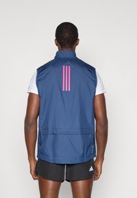 Navy sleeveless vest with a high collar and pink three-stripe logo on the back. Features a streamlined design and lightweight material.