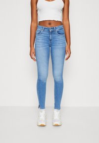 Ljust blå smala jeans med en klassisk femficksdesign, med en medelhög midja och sprund vid anklarna. Materialet verkar slätt och elastiskt.