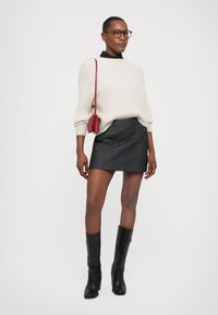 Gebreide crèmekleurige trui, zwarte blouse eronder, grijze spijkerrok, zwarte kniehoge laarzen, kleine rode schoudertas.