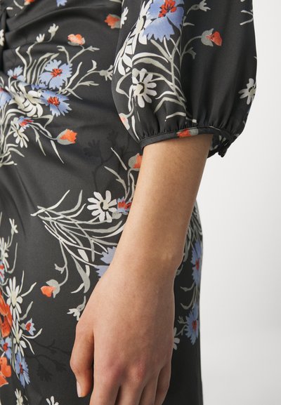 Blumenkleid aus schwarzem Stoff mit weißen, blauen und roten Blumen. Puffärmel und eine glatte Textur. Nahaufnahme des Ärmels und des Arms.
