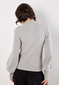Hellgrauer gestrickter Pullover mit hohem Kragen, strukturierter Stoff, Ballonärmel und gerippter Saum, von hinten betrachtet.