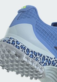 Blue athletic shoe featuring a textured upper, white sole with blue leopard print accents, and a green logo patch at the heel.