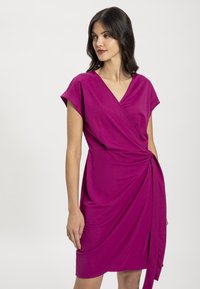 Fuksiapinkki kietaisumekko lyhyillä hihoilla, V-pääntiellä ja poimutetulla sivuyksityiskohdalla. Valmistettu kevyestä kankaasta, jossa on sileä rakenne.