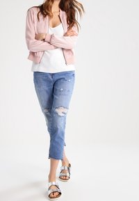 Roze satijnen bomberjack over een witte top, gecombineerd met gescheurde lichtblauwe spijkerbroek. Zilveren sandalen met brede bandjes. Casual outfit.