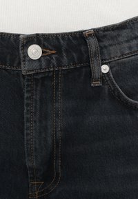 Tumši zili džinsi no dēnima ar šauru piegriezumu, redzamas kontrastējošas oranžas šuves, metāla pogas aizdare un klasiskas piecu kabatu dizains.