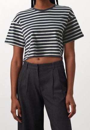 Personne portant un t-shirt court rayé horizontal noir et blanc associé à un pantalon plissé gris foncé taille haute.