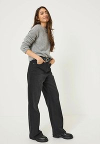 Maglione grigio a maglia, jeans neri a gamba larga con cintura e stivaletti neri robusti. Texture liscia, design classico e palette di colori neutri.