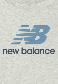 Blå New Balance-logo med stiliseret "NB" og teksten "new balance" på en lys grå stofbaggrund.