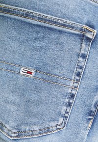 Bolsillo de jeans de mezclilla azul claro con costuras amarillas y un pequeño logotipo de la marca bordado en rojo, blanco y azul.