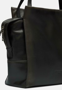 Czarna skórzana torba o gładkiej fakturze, z zamknięciem na zamek błyskawiczny, strukturalnym designem i subtelnym logotypem z boku.