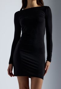Vestido negro de manga larga hecho de una tela elástica con una silueta ajustada y escote barco, que llega hasta la mitad del muslo. Textura suave.