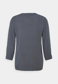 Grå långärmad skjorta med rund halsringning, uppvikta ärmar och en avslappnad passform. Tillverkad av slätt tyg med minimal sömnadsdetalj.