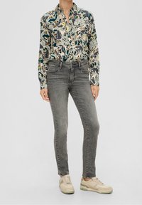 Camicia a maniche lunghe con bottoni, caratterizzata da un motivo floreale multicolore, abbinata a jeans slim fit grigi e sneakers beige con dettagli verdi.