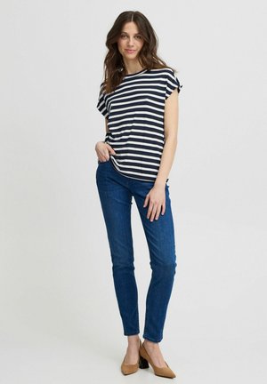 Tricou cu dungi albastre și albe, cu mâneci scurte, asortat cu blugi skinny albaștri și pantofi cu toc pătrat maro. Design simplu și casual.