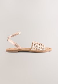 Platte sandaal met een bovenwerk van gevlochten stro in licht beige, een metalen enkelbandje, zachte tan voetbed en minimalistisch ontwerp. Gladde textuur.