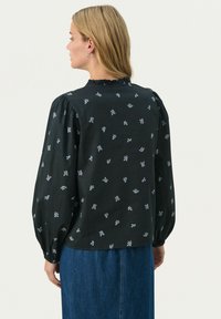 Czarna bluzka z teksturowej tkaniny, zdobiona niebieskimi kwiatowymi wzorami. Długie, bufiaste rękawy i falbaniasty dekolt. Klasyczny krój, casualowy design.