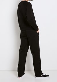 Felpa nera in cotone con collo a giro, polsini a coste e pantaloni della tuta neri coordinati. Presenta tasche a fessura e sneakers nere a contrasto.