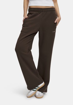 Brune sweatpants med en afslappet pasform, elastisk talje, sidelommer og subtil branding på benet. Parret med hvide sneakers.
