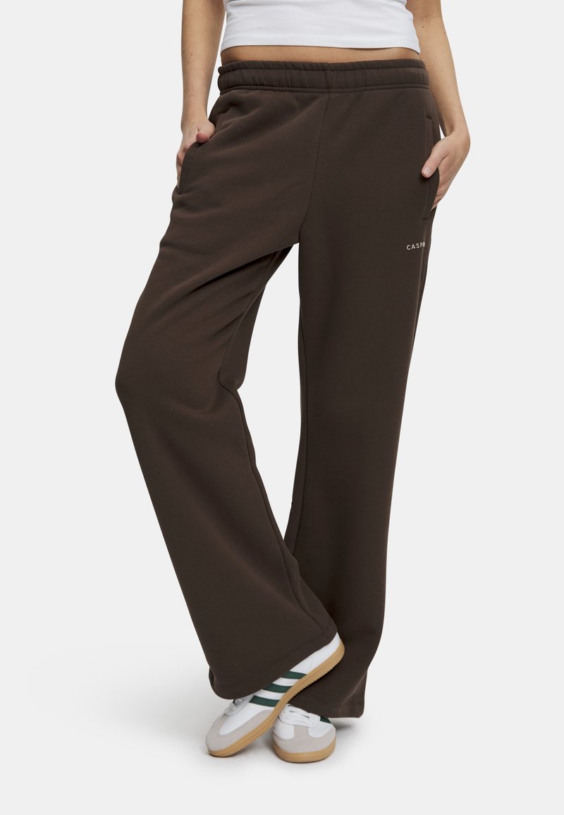 Bruna sweatpants med avslappnad passform, elastisk midja, sidofickor och subtil logga på benet. Kombinerat med vita sneakers.