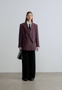 Prevelik bordo blazer z navpičnimi črtami, kombiniran s črnimi širokimi hlačami in majhno črno torbico. Gladek teksture z oprijetim ovratnikom.