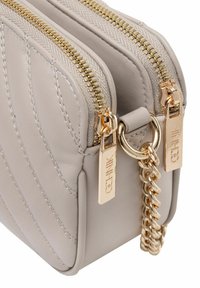 Szara skórzana torba z pikowanym wzorem, podwójnymi złotymi suwakami i złotym akcentem w postaci łańcucha. Posiada metalowe metki z nazwą marki.