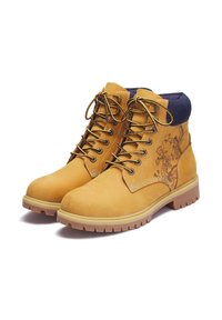 Ein Paar beigefarbene Arbeitsstiefel mit schwarzem Drachendesign an der Seite, dicken Gummisohlen, tanfarbenen und schwarzen Schnürsenkeln sowie einem gepolsterten blauen Kragen.