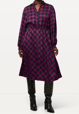 Kobieta w fioletowo-czarnej sukience midi w kratę z długimi rękawami oraz w czarnych, sięgających kolan, botkach na obcasie.