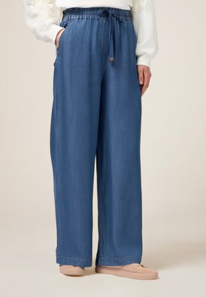 Pantaloni in denim blu chiaro a gamba larga con vita elastica e lacci. Presentano tasche laterali e una vestibilità comoda, abbinati a scarpe beige.