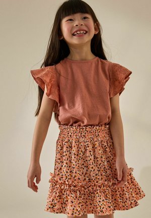 Top arancione chiaro con maniche in pizzo a volants abbinato a una gonna rosa a fantasia con vita smock e orlo a volants.