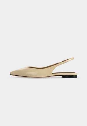 Zapato plano beige con puntera puntiaguda, diseño slingback, tacón bajo negro y acabado en cuero liso, mostrado de perfil sobre un fondo liso.