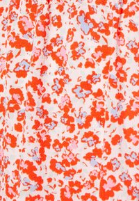 Tissu en coton blanc avec un motif floral rouge et bleu clair, présentant une surface texturée avec de petites fleurs disséminées partout.