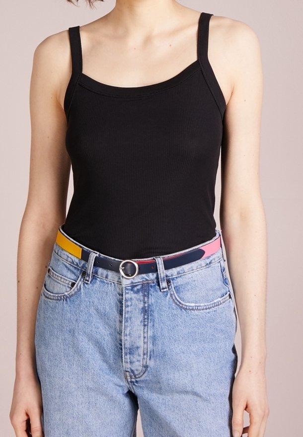 Femme portant un débardeur noir ajusté rentré dans un jean taille haute bleu clair avec une ceinture colorée.