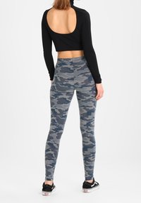 Grå camouflageleggings med blå detaljer, elastiskt tyg, kombinerat med en svart långärmad tröja med öppen ryggdesign. Svarta canvas skor.