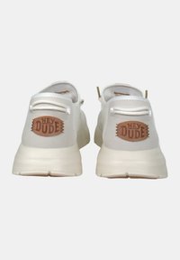 Sneakers bianchi con una texture liscia, caratterizzati da un logo in pelle marrone "HEY DUDE" sul tallone e un design minimalista con lacci elastici.