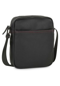 Bolso cruzado de cuero negro con una textura suave, que cuenta con un cierre con cremallera, costuras rojas y una correa ajustable para mayor comodidad.